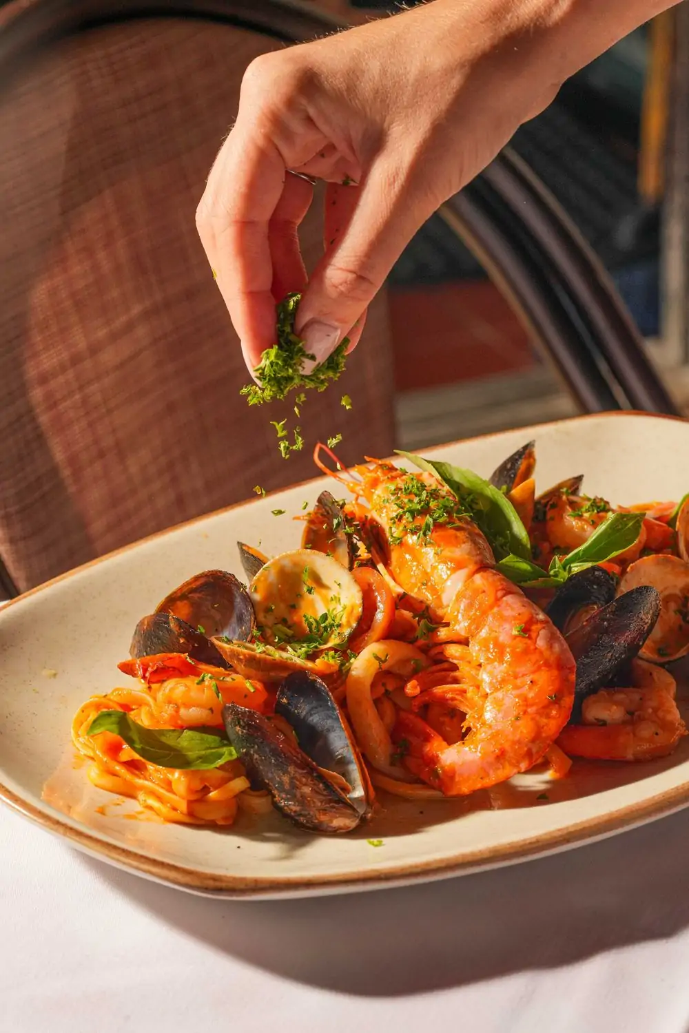 A hand sprinkles parsley over a plate of seafood fettuccini at Il Pastaiolo, a restaurant in Miami on OpenTable.
