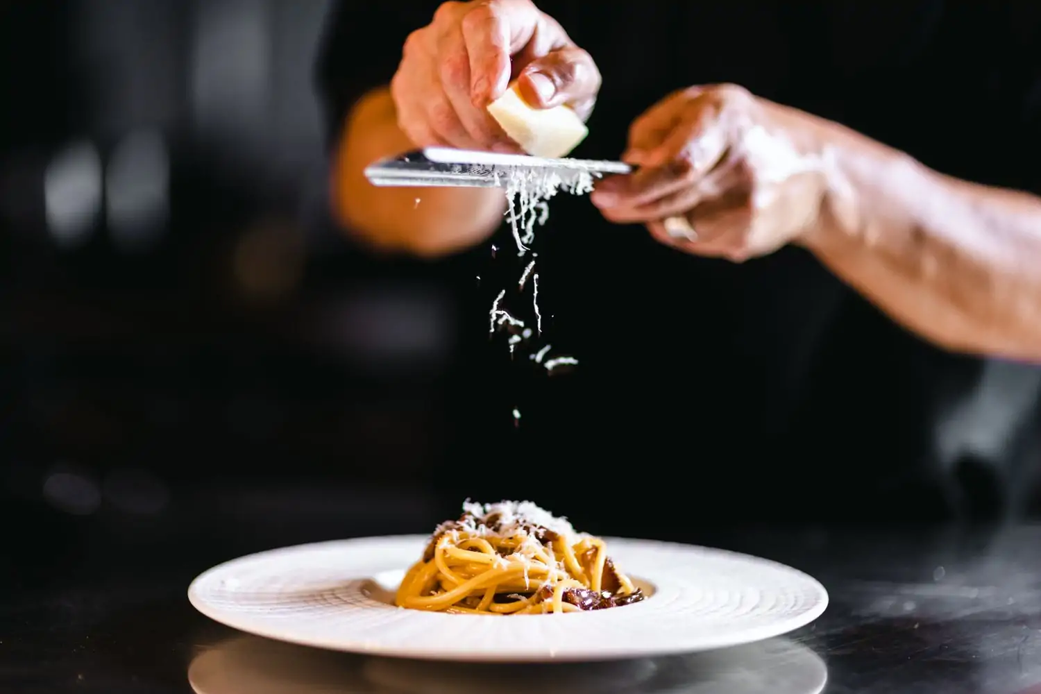 A server shaving parmesan over a plate of spaghetti at La Stella Cucina Verace, Dallas, a restaurant available on OpenTable.