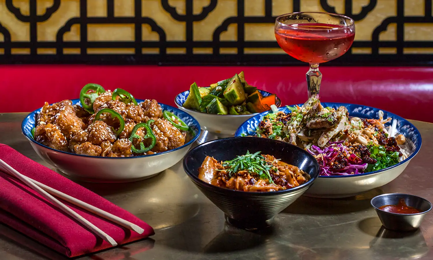 A table setting with different Chinese dishes, including orange chicken topped with sesame seeds, grilled vegetables, a salad, and more, with sweet and sour sauce, chopsticks, and a pink cocktail on the side at Formosa Cafe in Los Angeles, bookable via OpenTable.