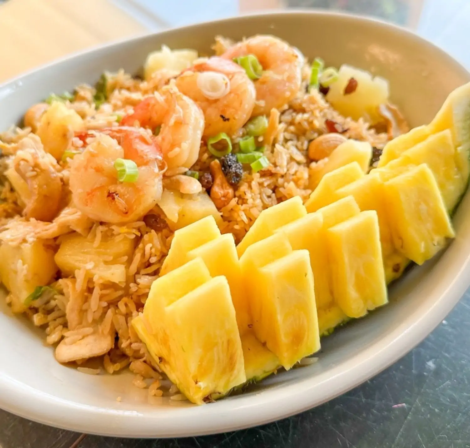 A white plate of pineapple fried rice topped with grilled shrimp, pineapple wedges, cashews, and green onions at Sirinat Thai & Sushi Bar in San Pedro, Los Angeles, available to book on OpenTable.