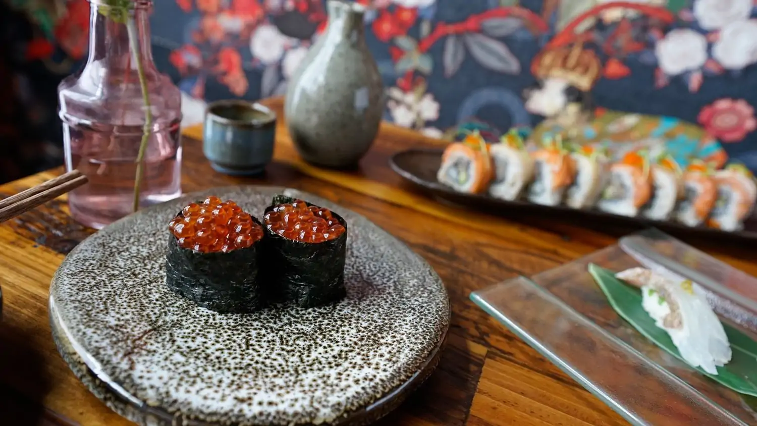 A wall painted with flowers in blue, red, and white, a wooden table holds saki and platters of sushi. This OpenTable selection is one of the best restaurants in Venice Beach, Los Angeles.