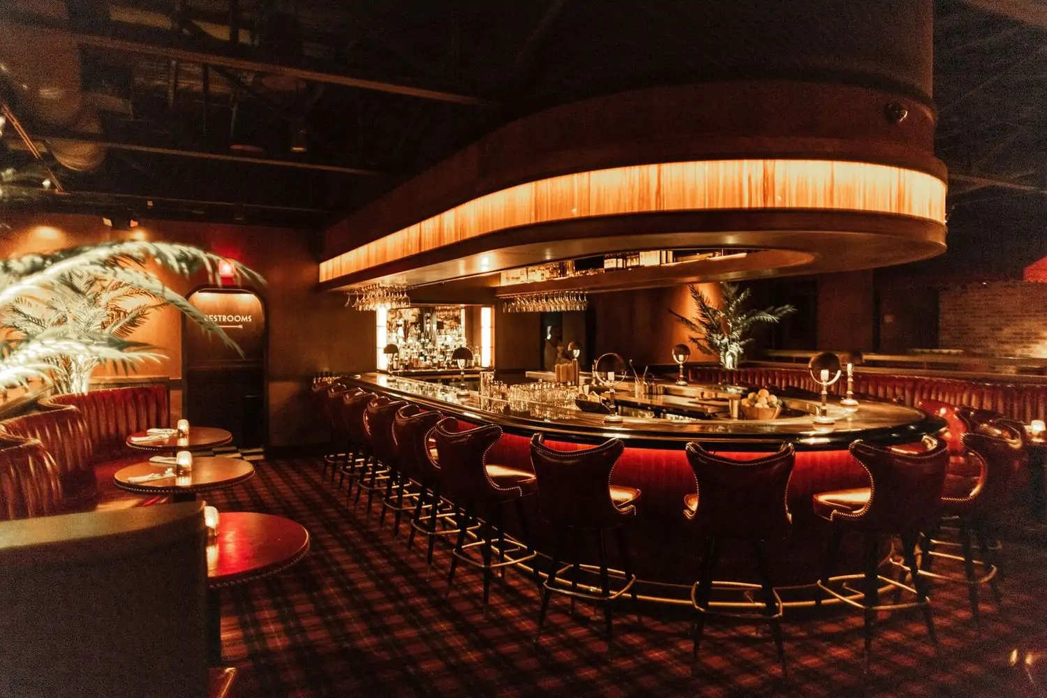 A sultry lounge with red leather sofas, dim lighting, and a central bar with high-back, leather stools at Drake's Hollywood, one of the best cozy restaurants in Dallas on OpenTable