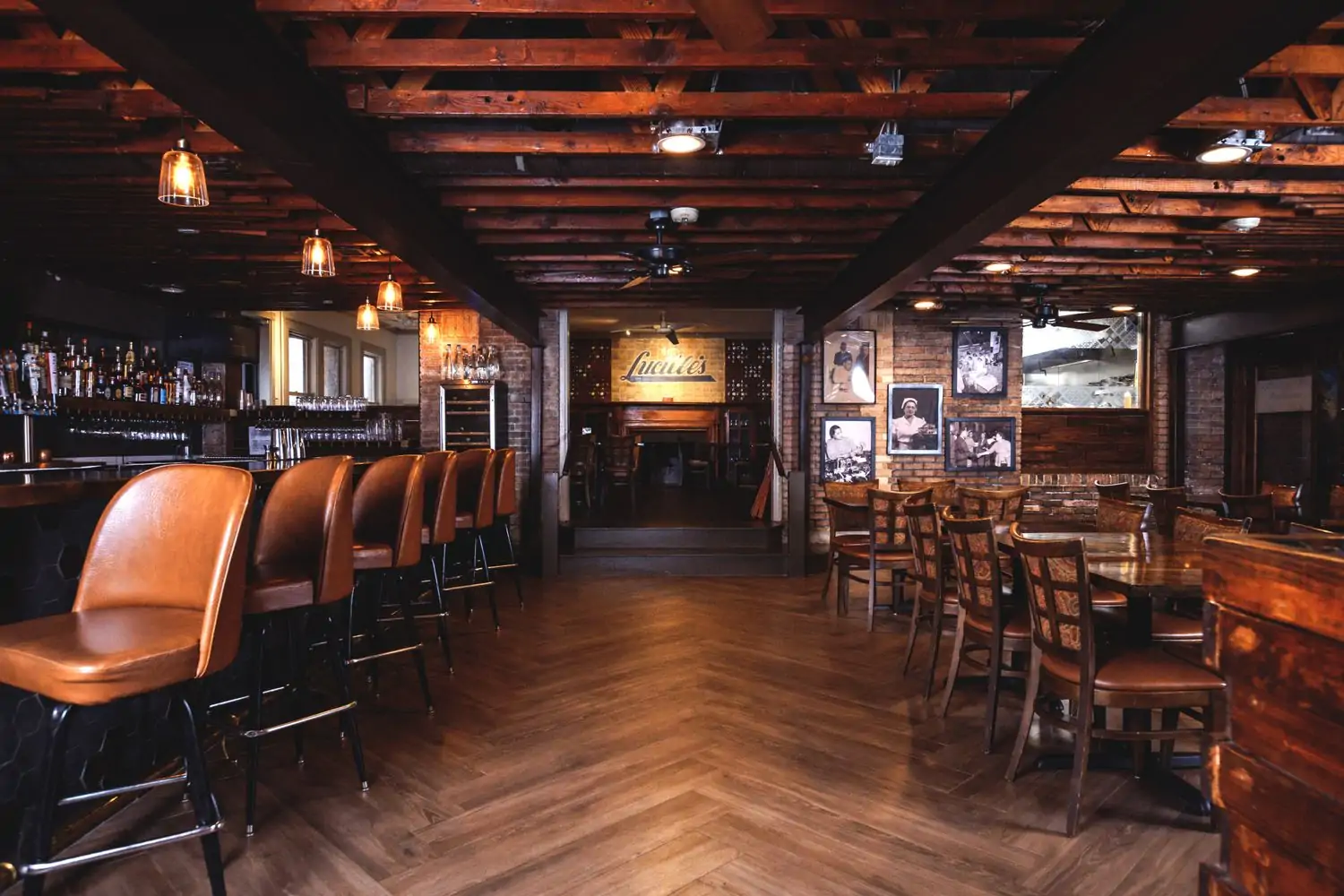 A dining room with dark wood paneling on both the floor and ceiling with brown cushioned chairs and a full bar at Lucille’s, one of the best cozy restaurants in Houston, bookable on OpenTable.