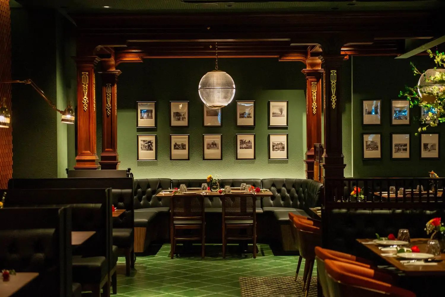 A dimly lit, upscale restaurant interior with dark wood paneling, green walls, and a collection of framed photographs with plush booths, tables, and chairs at Star Leaf - Asian Cuisine, one of the best Thai restaurants in Los Angeles available to book on OpenTable.