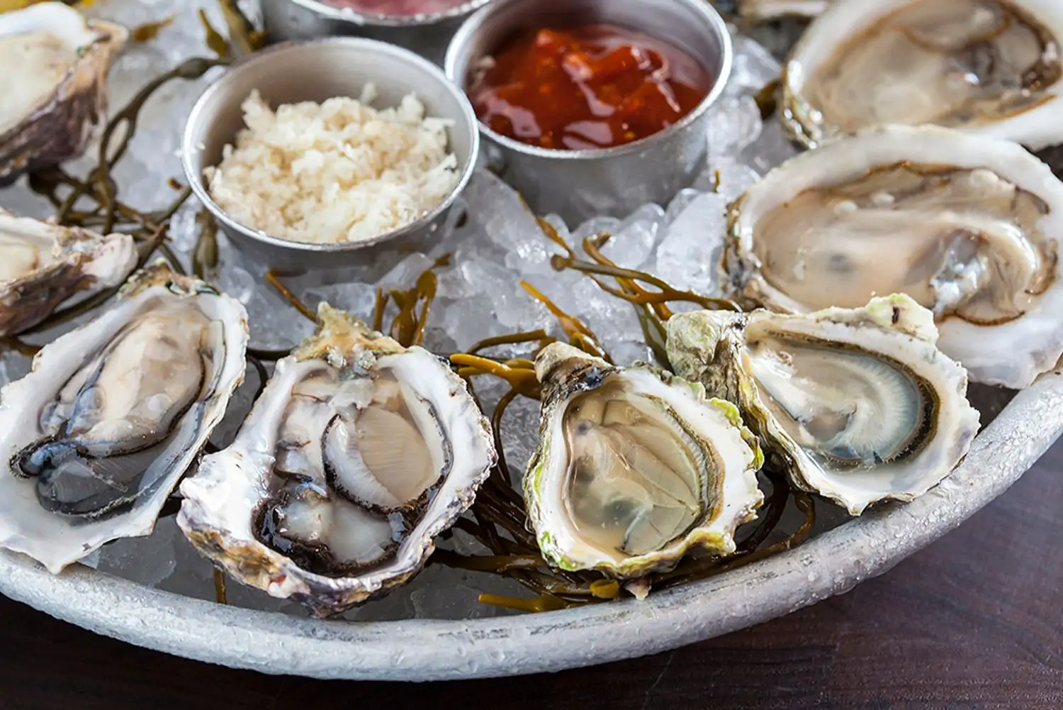 A plate of a dozen oysters on the half shell chilled on ice with horseradish and a tomato-based sauce at King’s Fish House - Calabasas, in Los Angeles, on OpenTable.