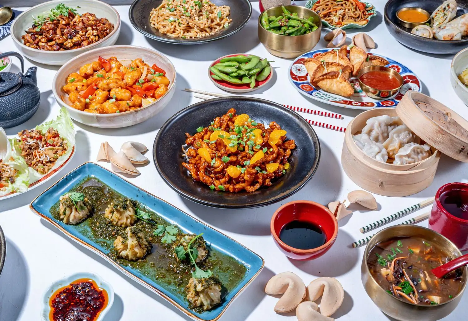 A table setting featuring plenty of shareable plates like edamame, soups, orange chicken, dumplings, sauces, and fortune cookies at Chin Chin, a Chinese restaurant in Los Angeles found on OpenTable.