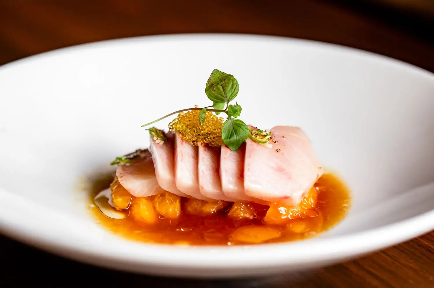 A plate of thinly sliced raw fish, arranged in a circular pattern, with a bed of orange sauce and garnished with caviar and herbs on a white plate at Uchi, one of the best birthday restaurants Los Angeles available to book on OpenTable.