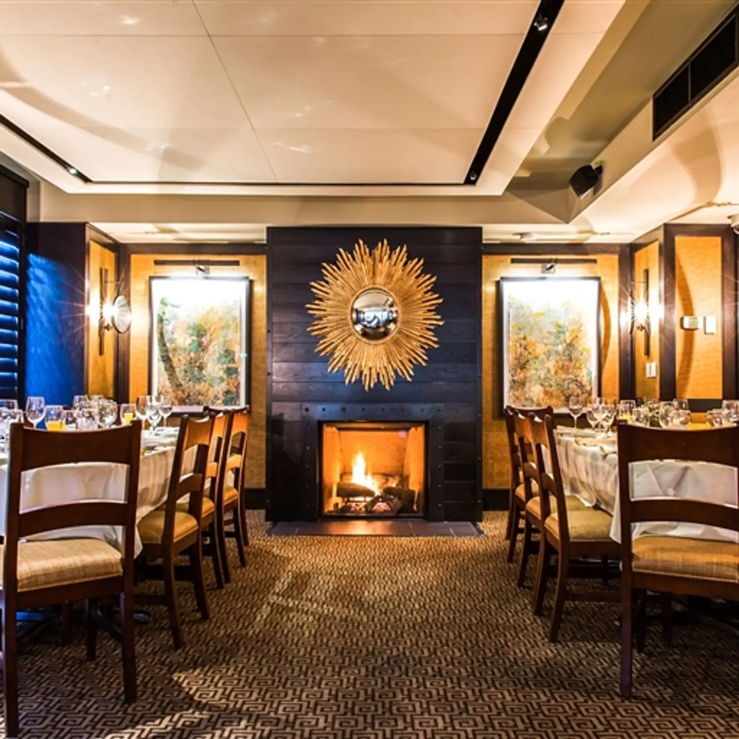 A carpeted dining room with a golden Art Deco mirror shaped like a sun hanging over a fireplace with two long, rectangular tables covered in white tablecloths at Harvest in Boston, on OpenTable.