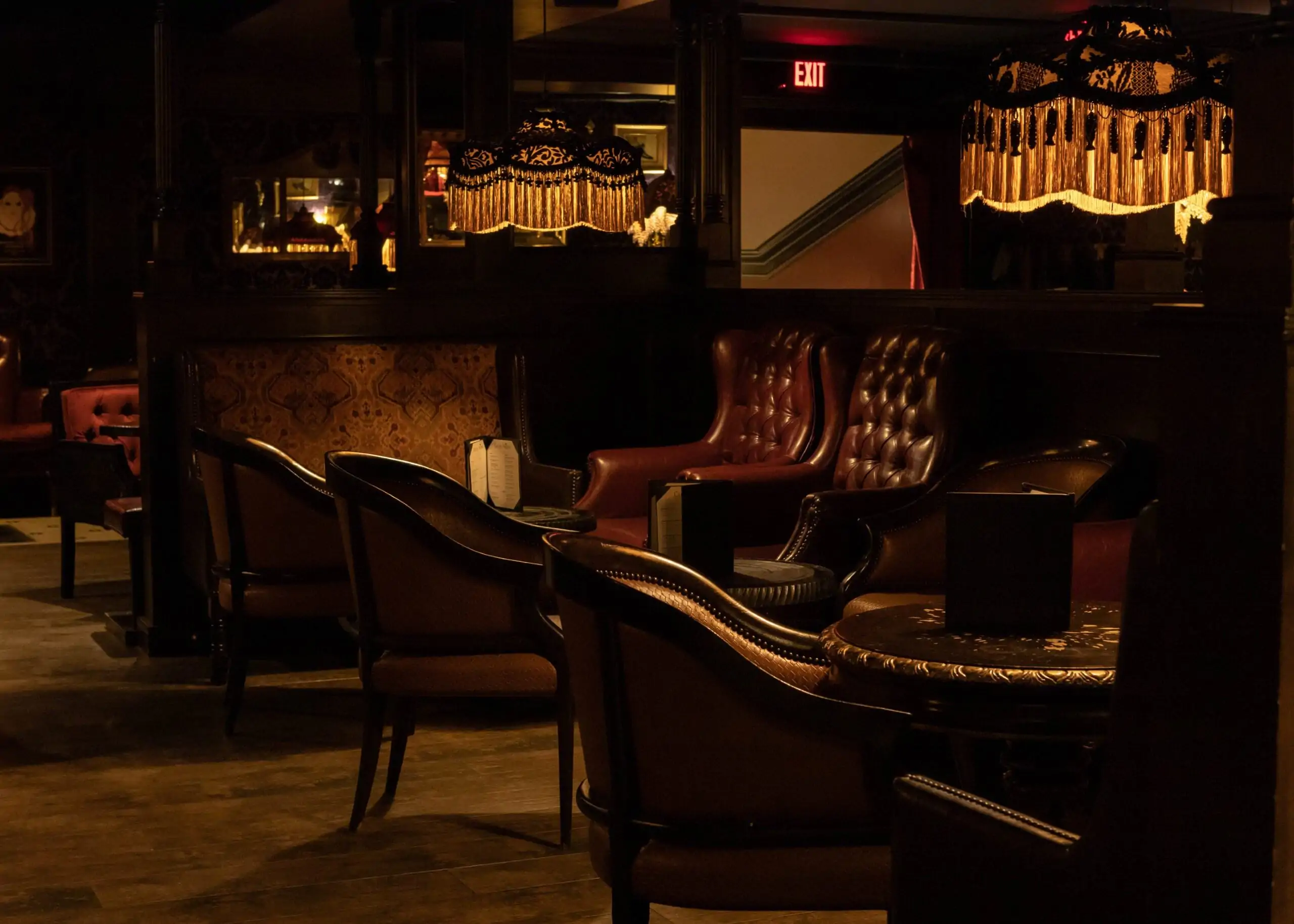 A polished wooden bar with red leather-topped stools and circular light fixtures casting a warm glow over the bottles of spirits at Carrie Nation, one of the best cozy restaurants in Boston on OpenTable.