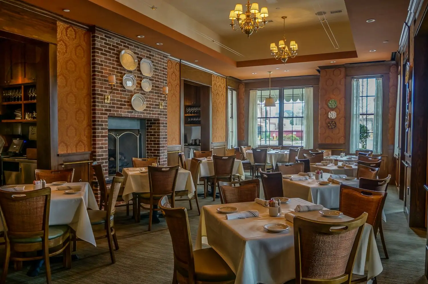 A dining room with warm gold and brown furnishings, white tablecloths, large windows, and a fireplace at Grace’s, one of the best Houston restaurants with fireplaces found on OpenTable.
