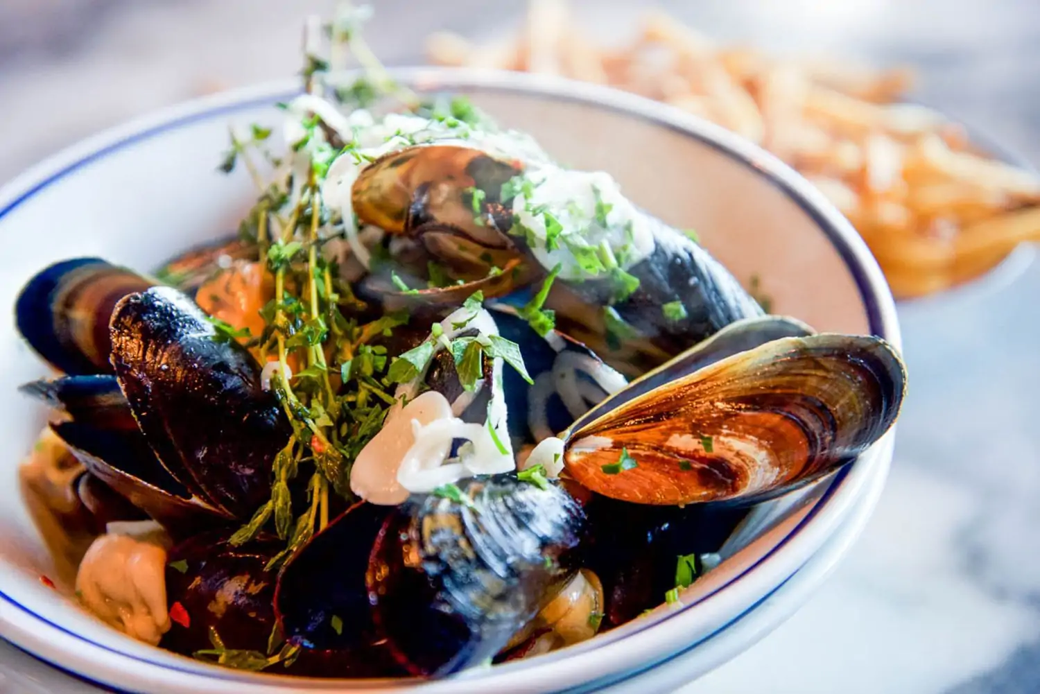 A white bowl with a blue lined rim of moules frites, one of the classic dishes at Petit Trois L’Original in Los Angeles, available to book on OpenTable.