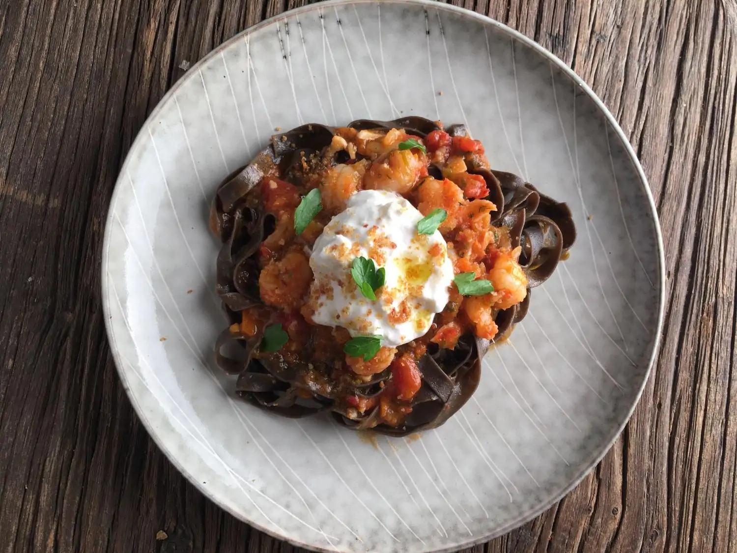 A plate of black squid ink pasta topped with a creamy sauce, fresh scallops, and a dollop of burrata cheese at Jame, an Italian restaurant in El Segundo, Los Angeles, available to book on OpenTable.