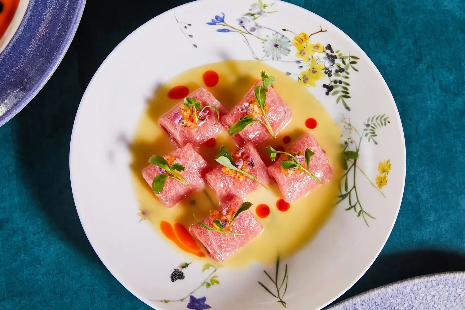 A white plate with six rolled pieces of uncooked fish topped with floral garnishes served in a light yellow broth at Catch LA, one of the best fish restaurants in Los Angeles, on OpenTable.