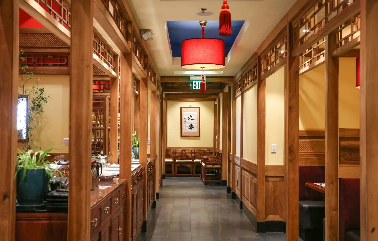 A bright dining room with light wood decor and traditional red Chinese lamps, and a picture of Chinese lettering on the back wall at Bistro Na’s, a Chinese restaurant in Los Angeles, available on OpenTable.