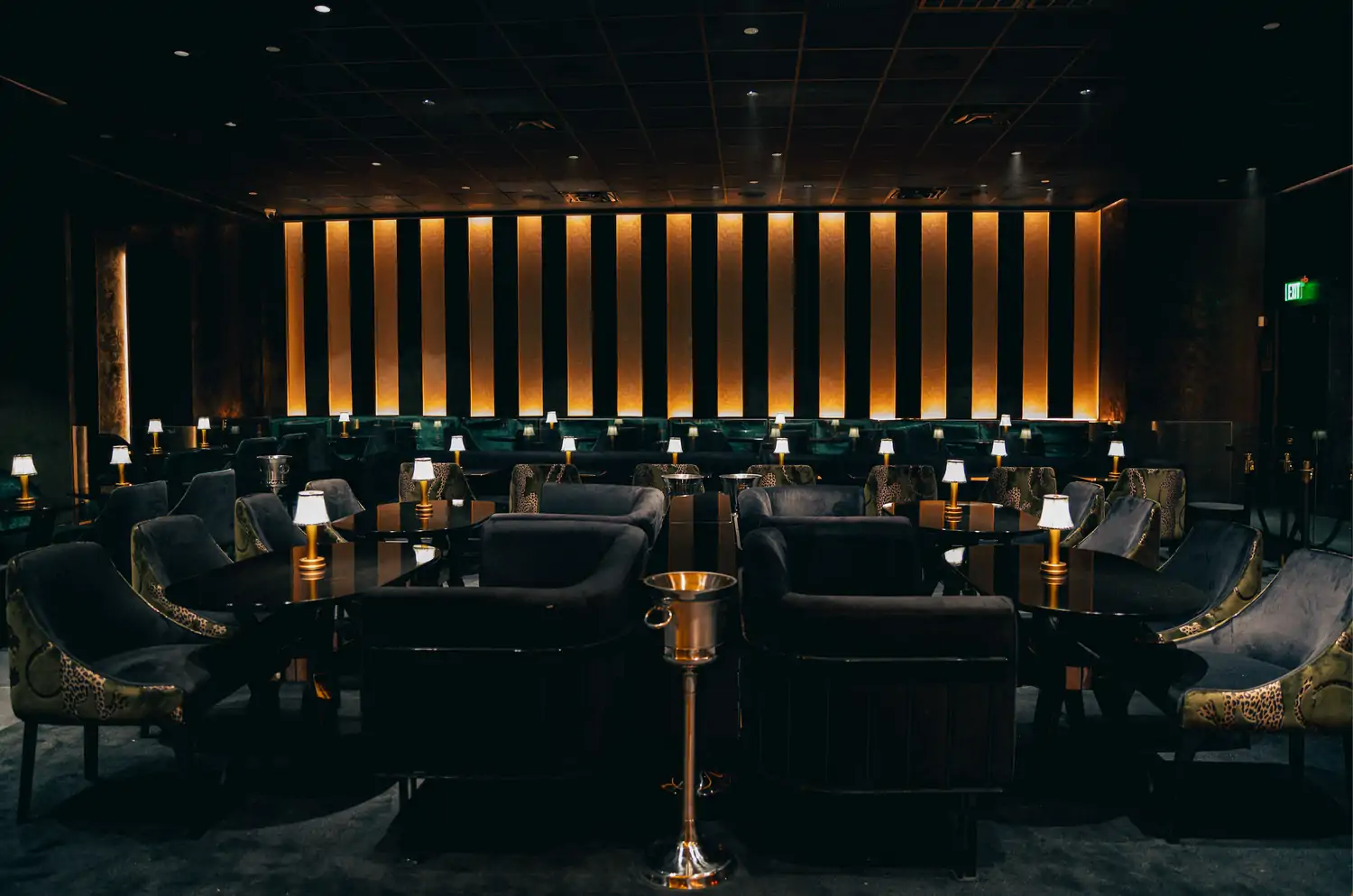 A dimly lit lounge with floors carpeted in black and lounge chairs and sofas with emerald and gold detailing at Regines Lounge, one of the best cozy restaurants in Dallas, on OpenTable.
