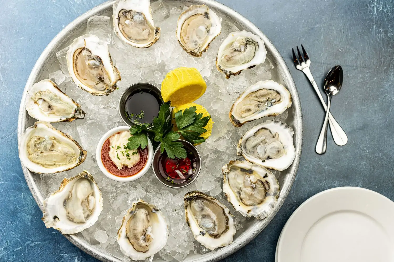 A plate of a dozen oysters on the half shell with horseradish, vinegar, and slices of lemon at Neighborhood Services in Dallas. Book on OpenTable.