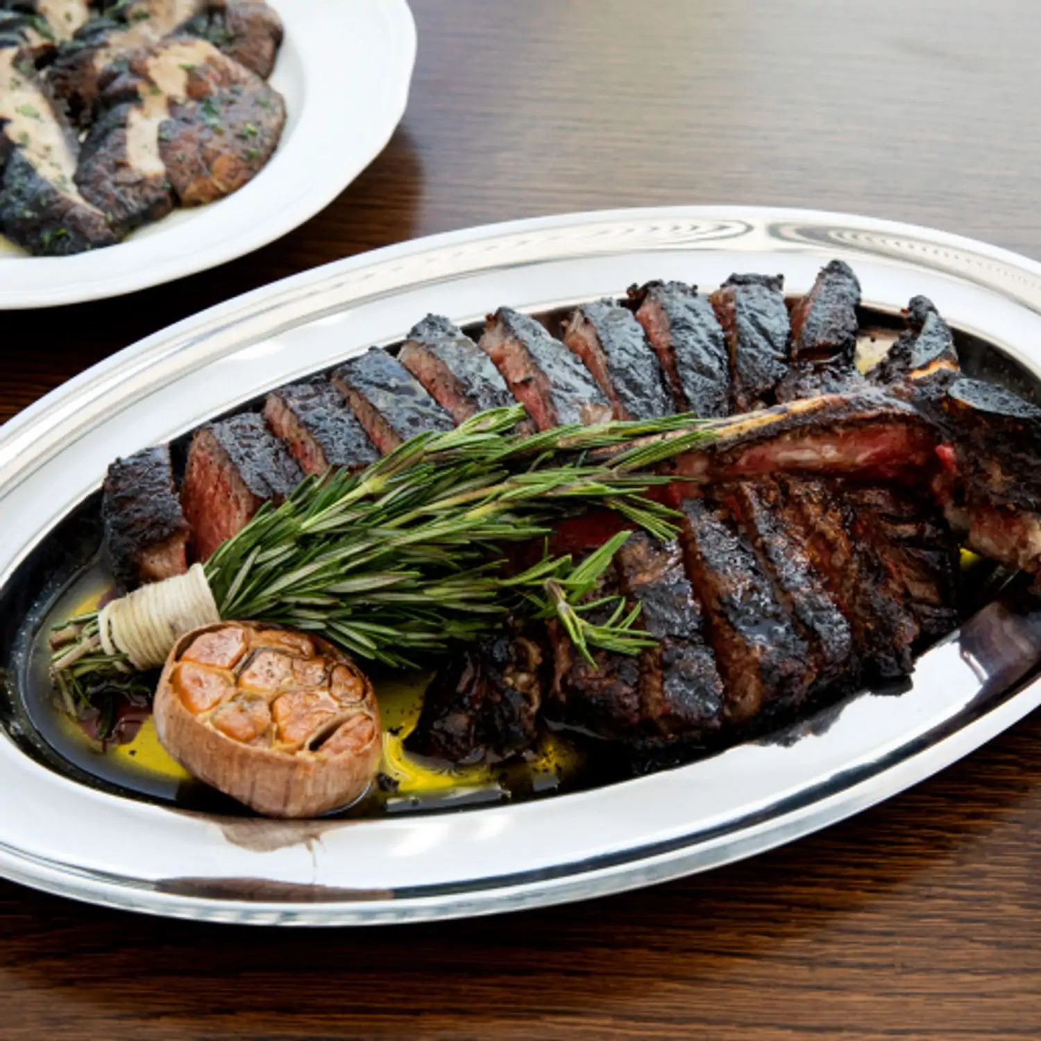 A metal serving tray with bistecca fiorentina, rosemary, and half a head of garlic at Contessa – Miami, a Miami restaurant available via OpenTable.
