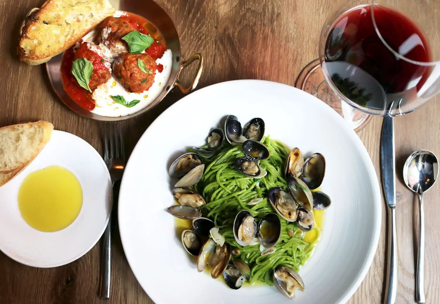 Bread and olive oil, meatballs in tomato sauce and mozzarella, a plate of green pasta with clams in the shell, and a glass of red wine await you at Marmo in Montrose, Houston, bookable on OpenTable.