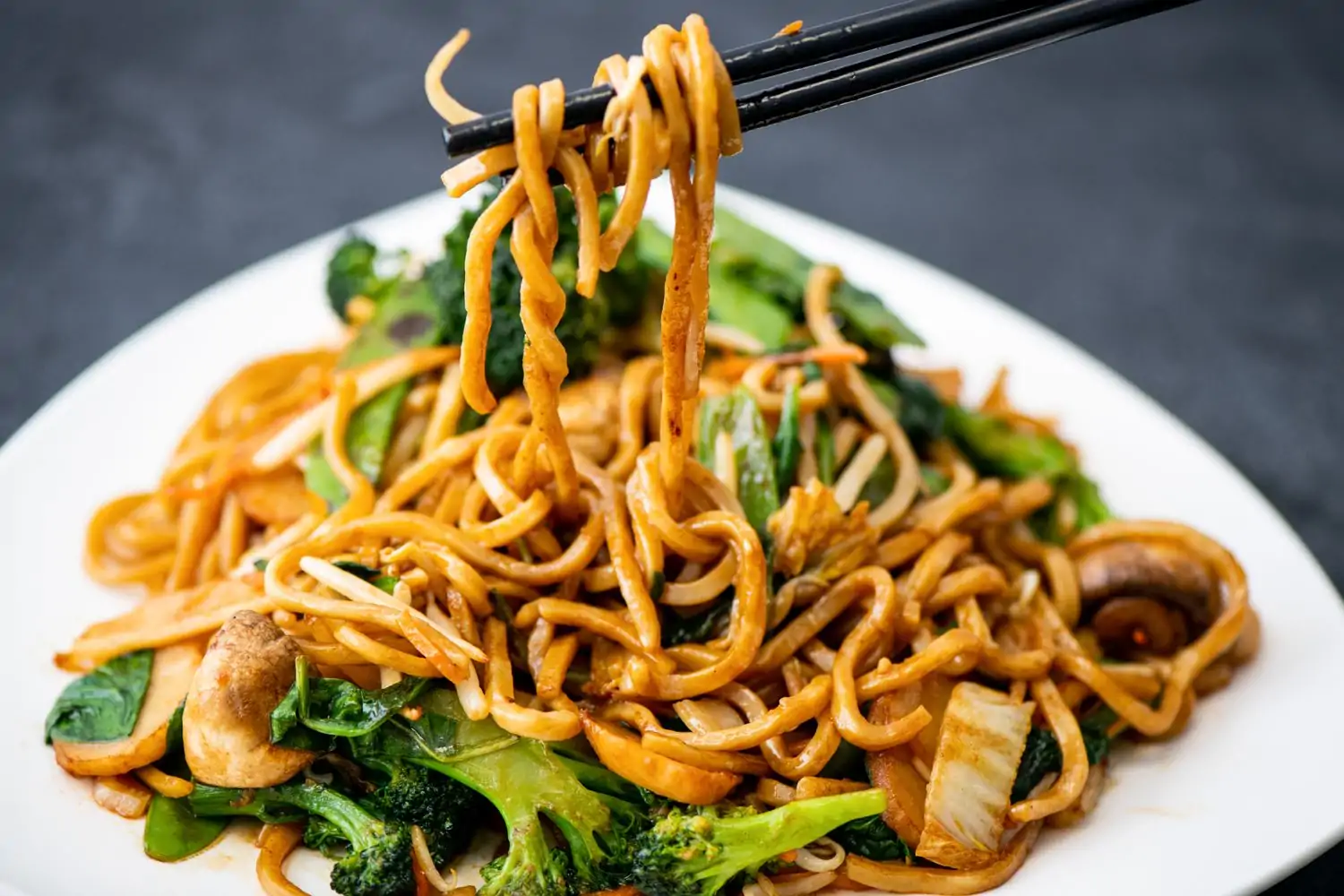 A plate with Chinese noodles, grilled mushrooms, and broccoli, with a pair of chopsticks holding some noodles above the plate at Panda Inn, a Chinese restaurant in Los Angeles bookable on OpenTable.