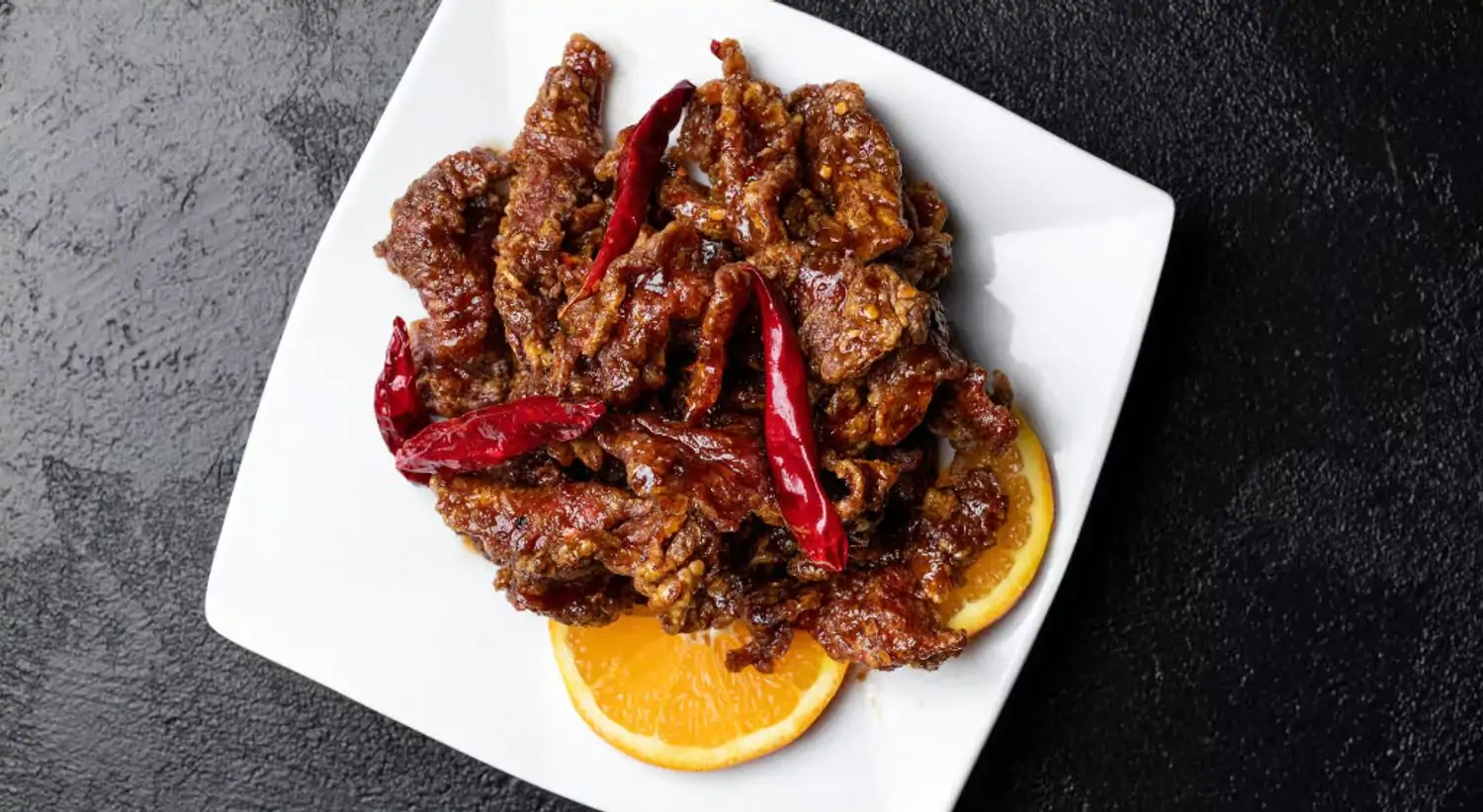 A plate containing fried chicken in savory sauce topped with red chili peppers and orange slices on the side at Joss Cuisine, one of the best Chinese restaurants in Los Angeles, bookable on OpenTable.