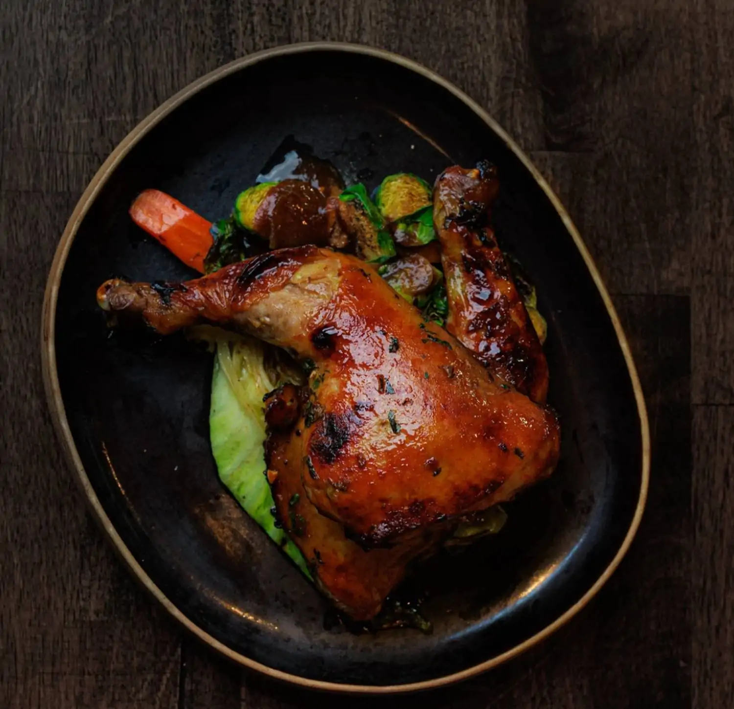 A plate of roasted chicken with crispy skin, served with roasted Brussels sprouts, carrots, and a side of cabbage at La Ong, one of the top Thai restaurants in Los Angeles on OpenTable.