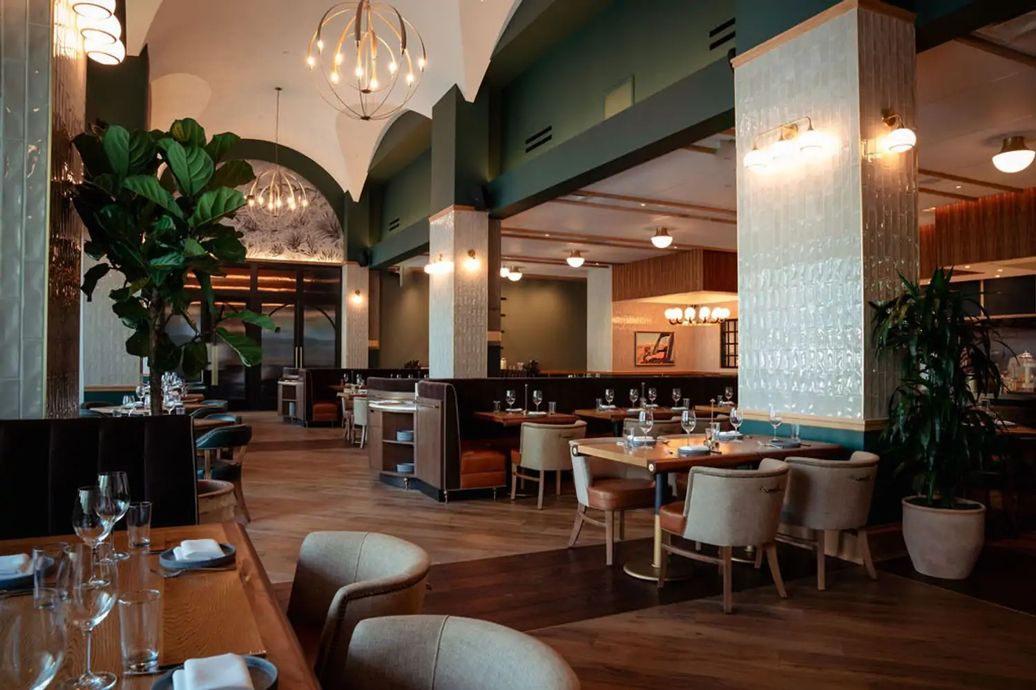 A dining room with light and dark wood floors, cushioned round chairs, and hunter green accenting and plants at Credence, one of the best cozy restaurants in Houston, found on OpenTable.