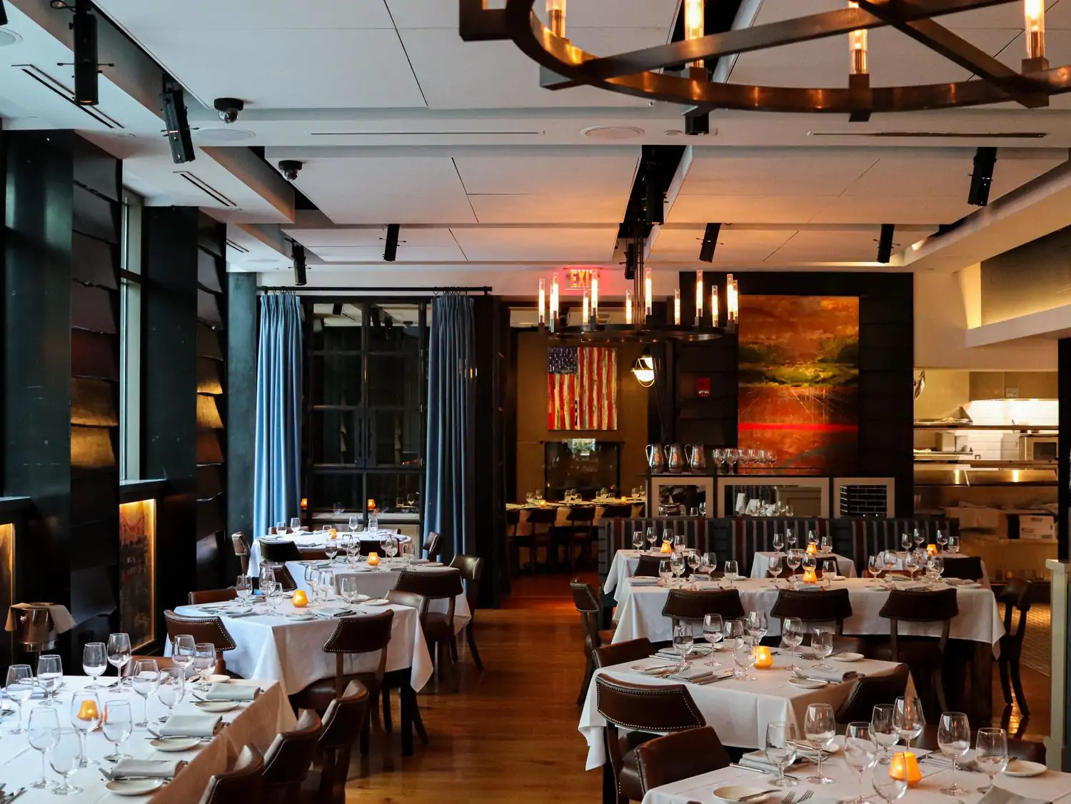The dining room at the Banks Seafood and Steak in Boston has dark wood floors, iron chandeliers, square and rectangular tables covered in white tablecloths, and floor-to-ceiling windows – book via OpenTable.