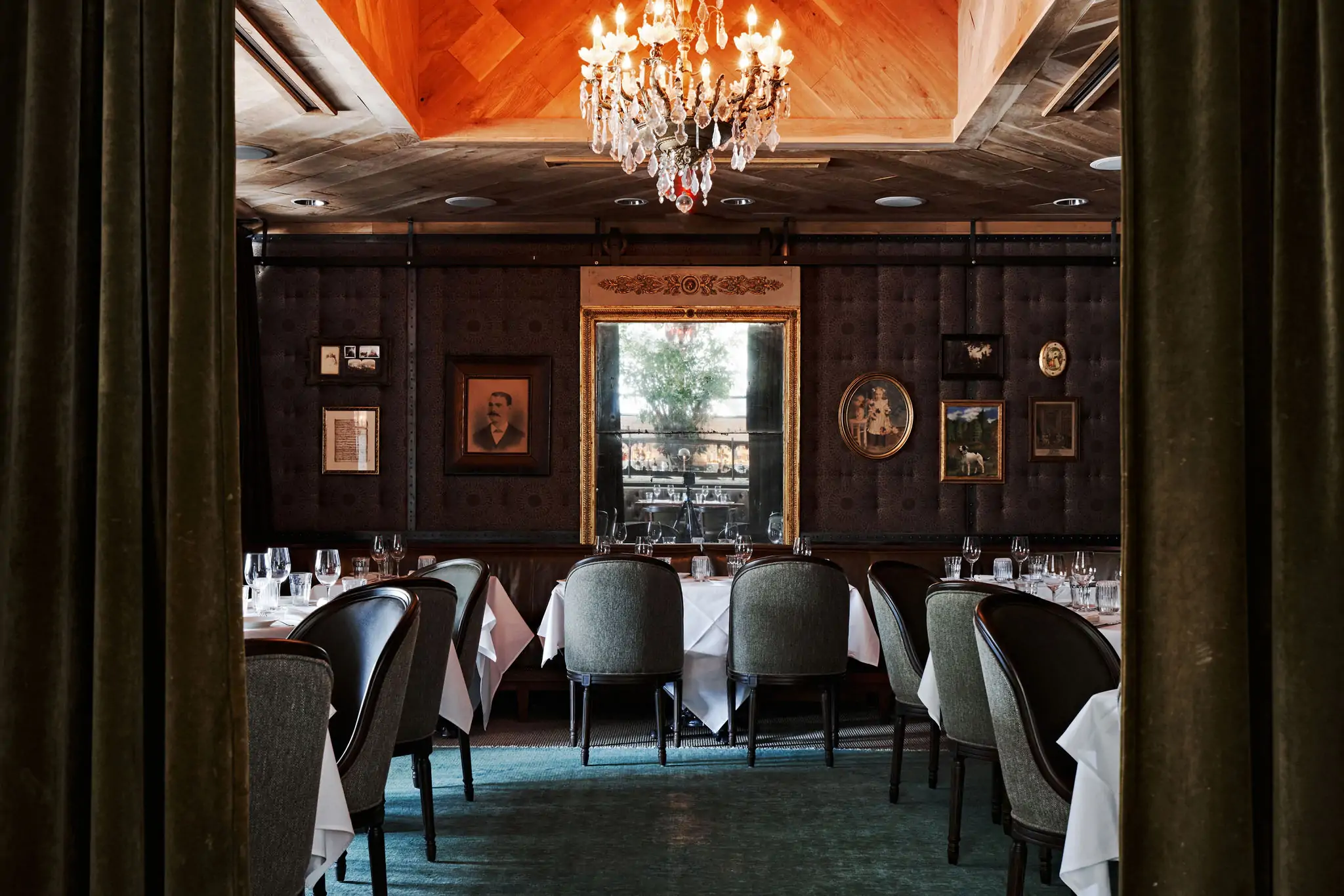 A dining room with tables and chairs, a wood-paneled wall with photos, and a chandelier at State of Grace, one of the best cozy restaurants in Houston, bookable on OpenTable.