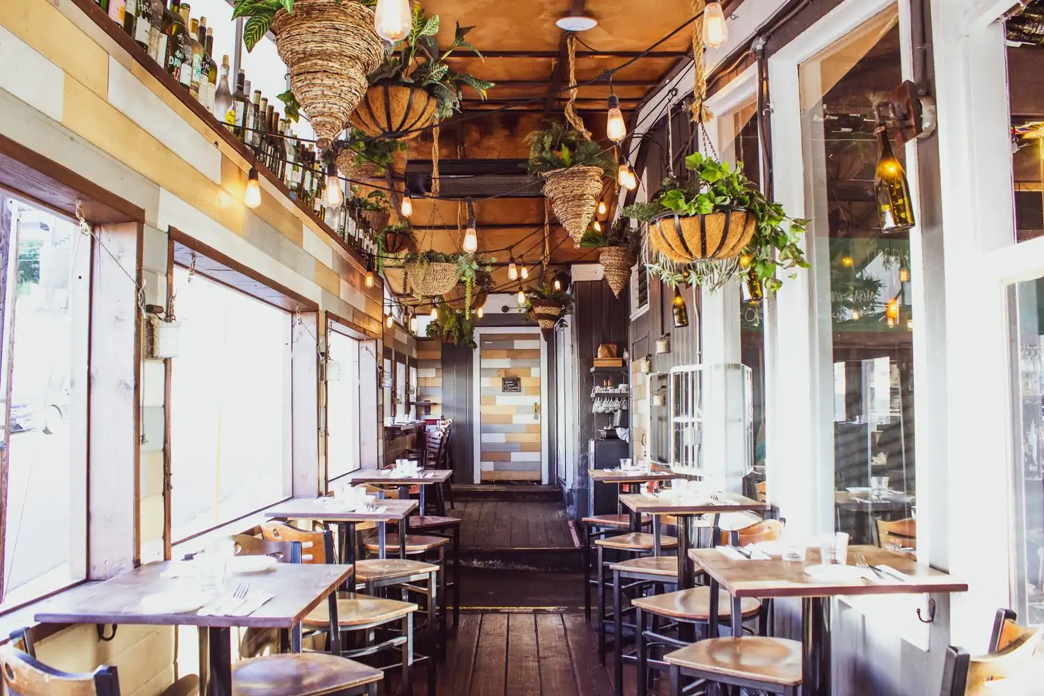 A cozy and inviting restaurant patio with wooden tables and chairs, string lights, and hanging plants at Bacari in Playa del Rey Los Angeles, now on OpenTable.