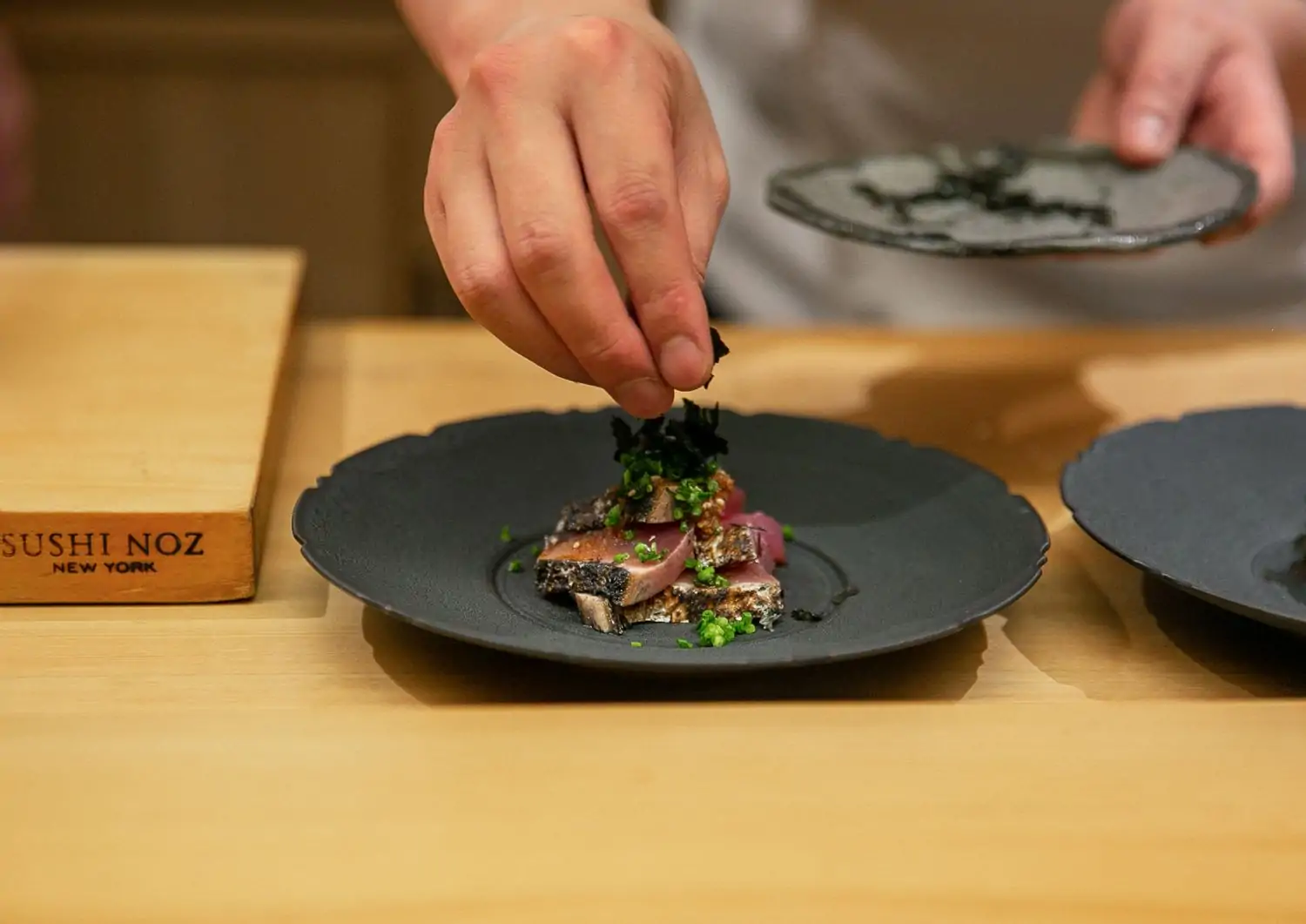 A pair of hands shown plating a sushi dish at New York restaurant Sushi Noz