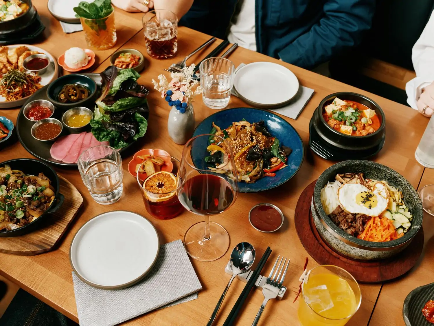 People gather around a table of banchan, large platters of Korean dishes like bibimbap, and colorful cocktails at Mister Tiger in Chicago available on OpenTable.