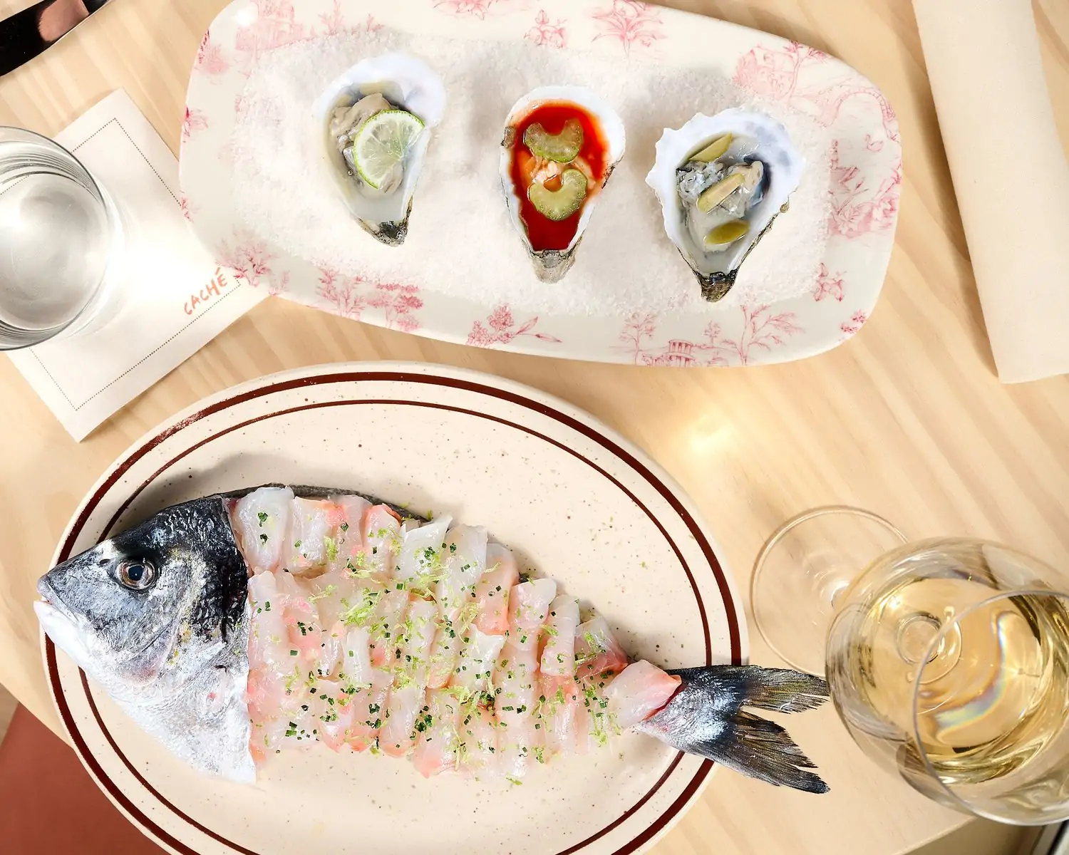 Three dressed oysters and a sea bream sashimi set into the shape of a fish with a glass of white wine at Caché, one of the best new restaurants in San Francisco on OpenTable.