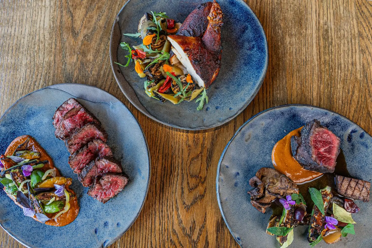Grilled meats, including chicken, placed on a wooden table at Austin restaurant Hestia