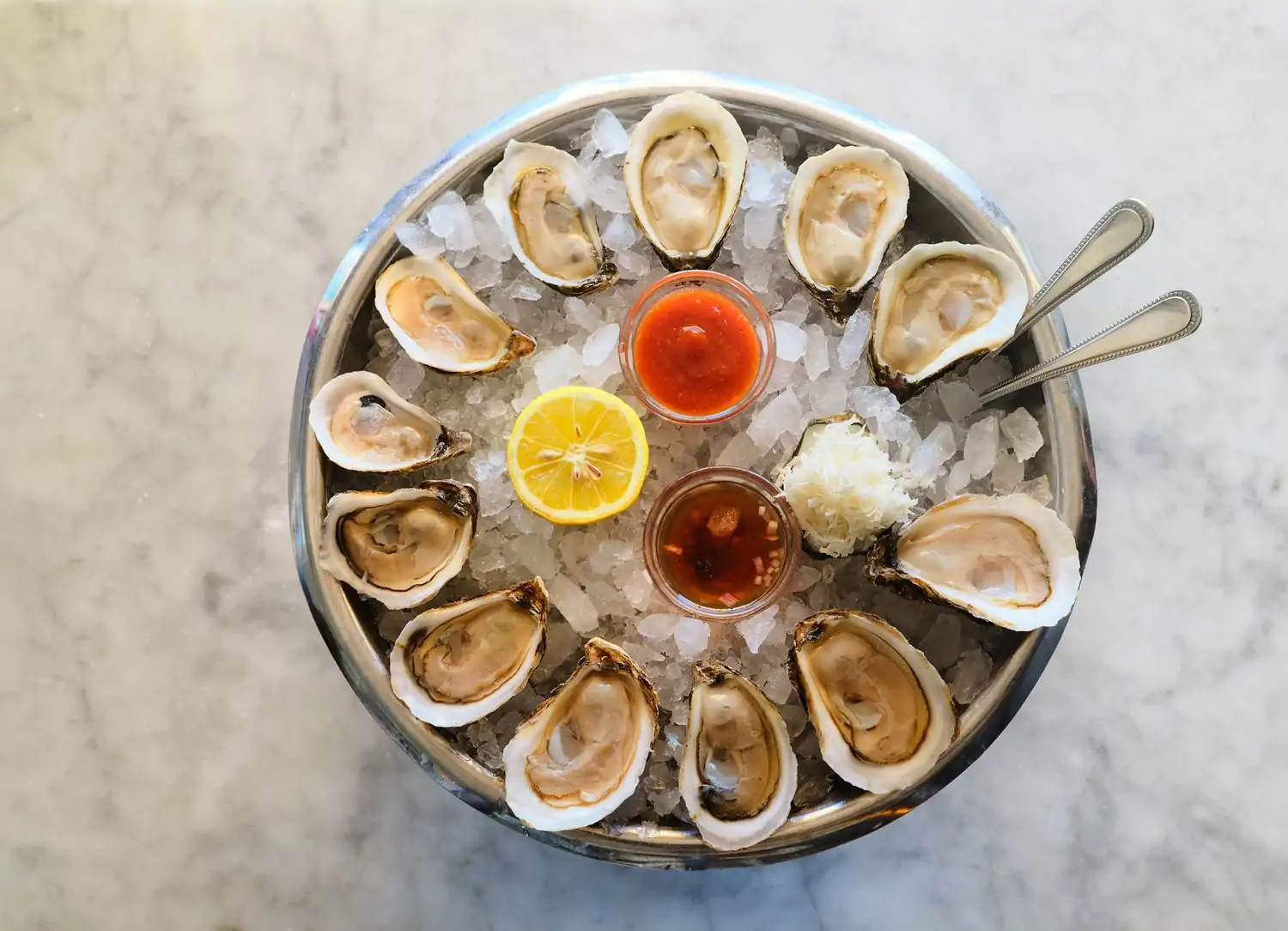A dozen raw oysters on ice with lemon wedge, hot sauce, and mignonette in the middle at Clark’s Oyster Bar in San Francisco. Book on OpenTable.