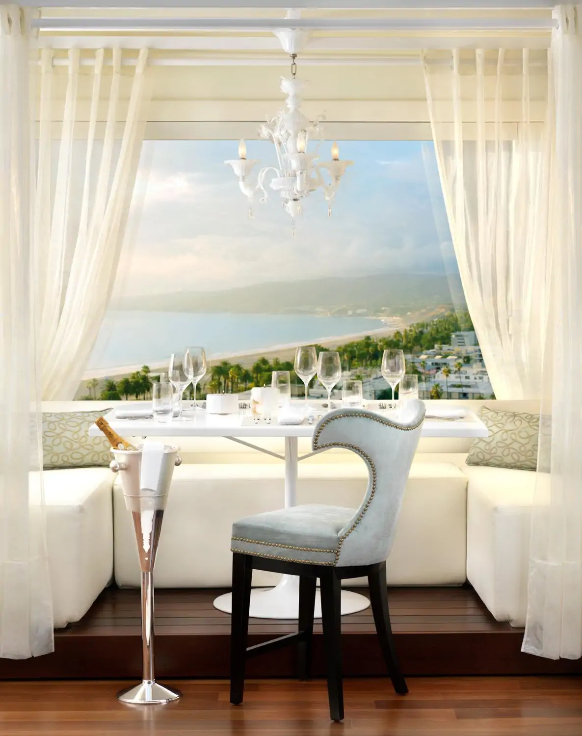 A romantic table setting for two with a white tablecloth, candles, and a champagne bucket overlooking a stunning ocean view at The Penthouse Restaurant, one of the best restaurants on the beach in Los Angeles, on OpenTable.