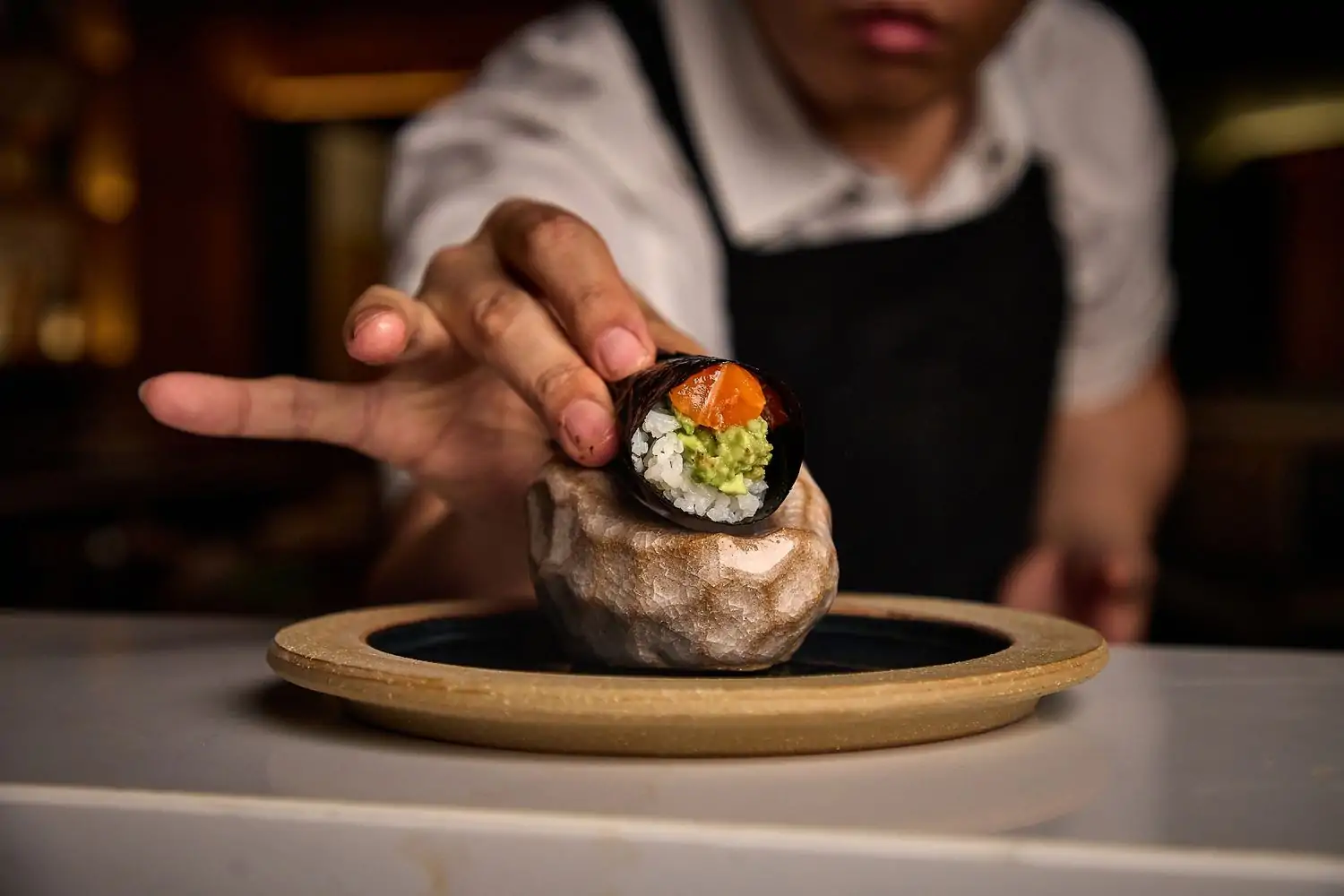 A person in a white shirt and black apron touches an elegant sushi roll at Noriko, one of the Chicago best new restaurants available on OpenTable.