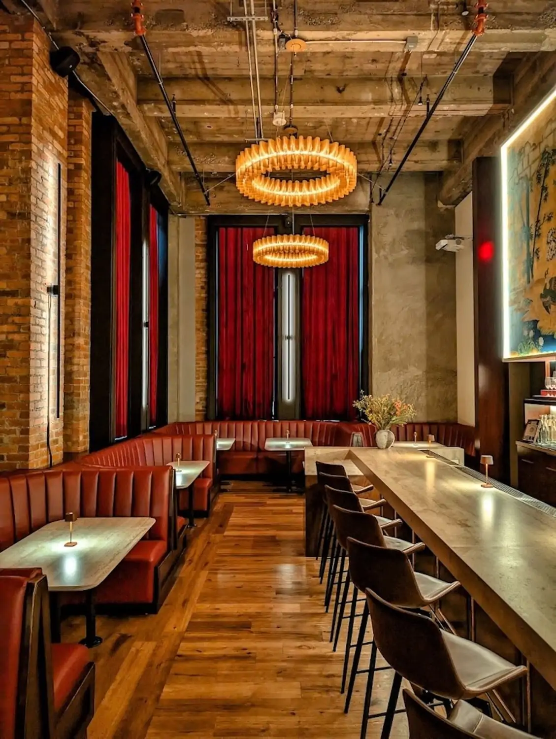 A brick-walled dining room with industrial ceilings, red curtains with a window, red banquets, and a long stone bar at Cafe Shoji Restaurant in San Francisco on OpenTable.
