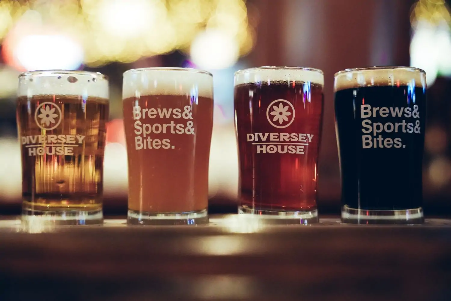 Four craft beers in Diversey House branded mugs against a blurry background at Diversey House, an OpenTable restaurant in Chicago.