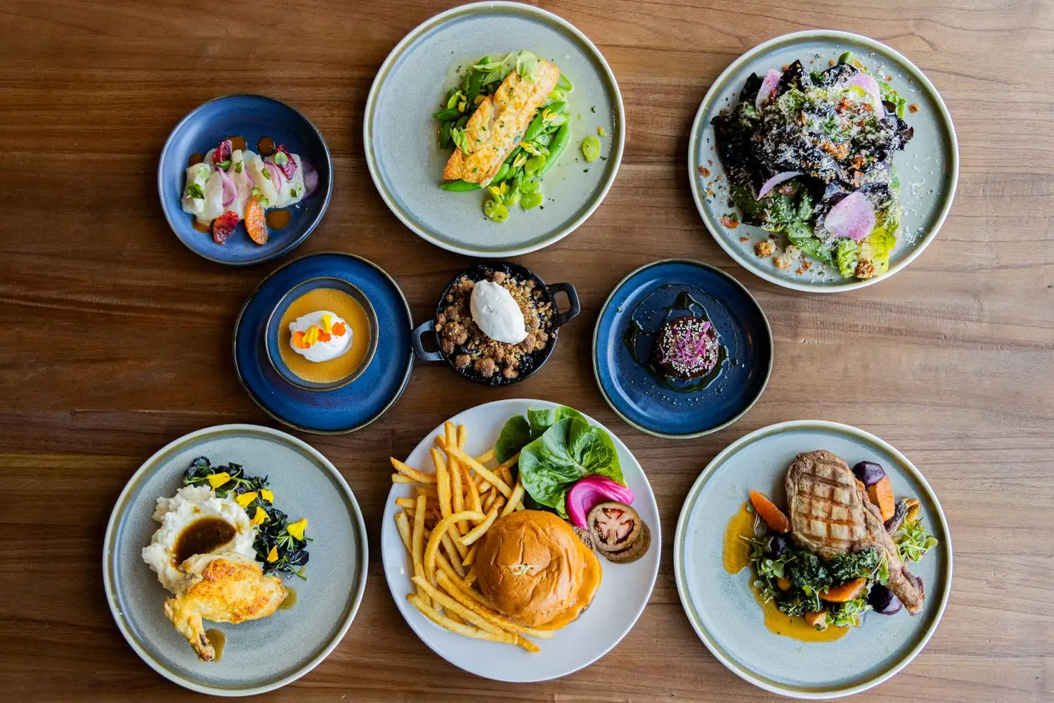 Several platters of items like a burger and fries, chicken and mashed potatoes, a green salad, blueberry cobbler, and more at Fifty Vara
