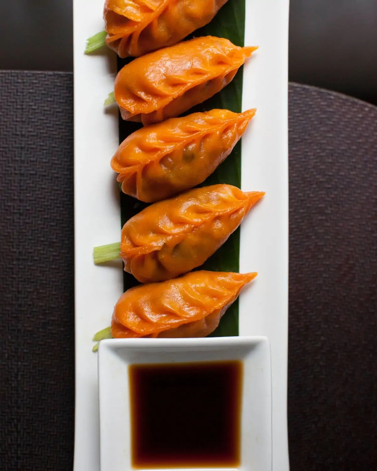 A white, rectangular plate holds a line of orange carrot dumplings with scallion and a side of dipping sauce at Buddakan, one of the best Chinese restaurants in NYC, bookable on OpenTable.
