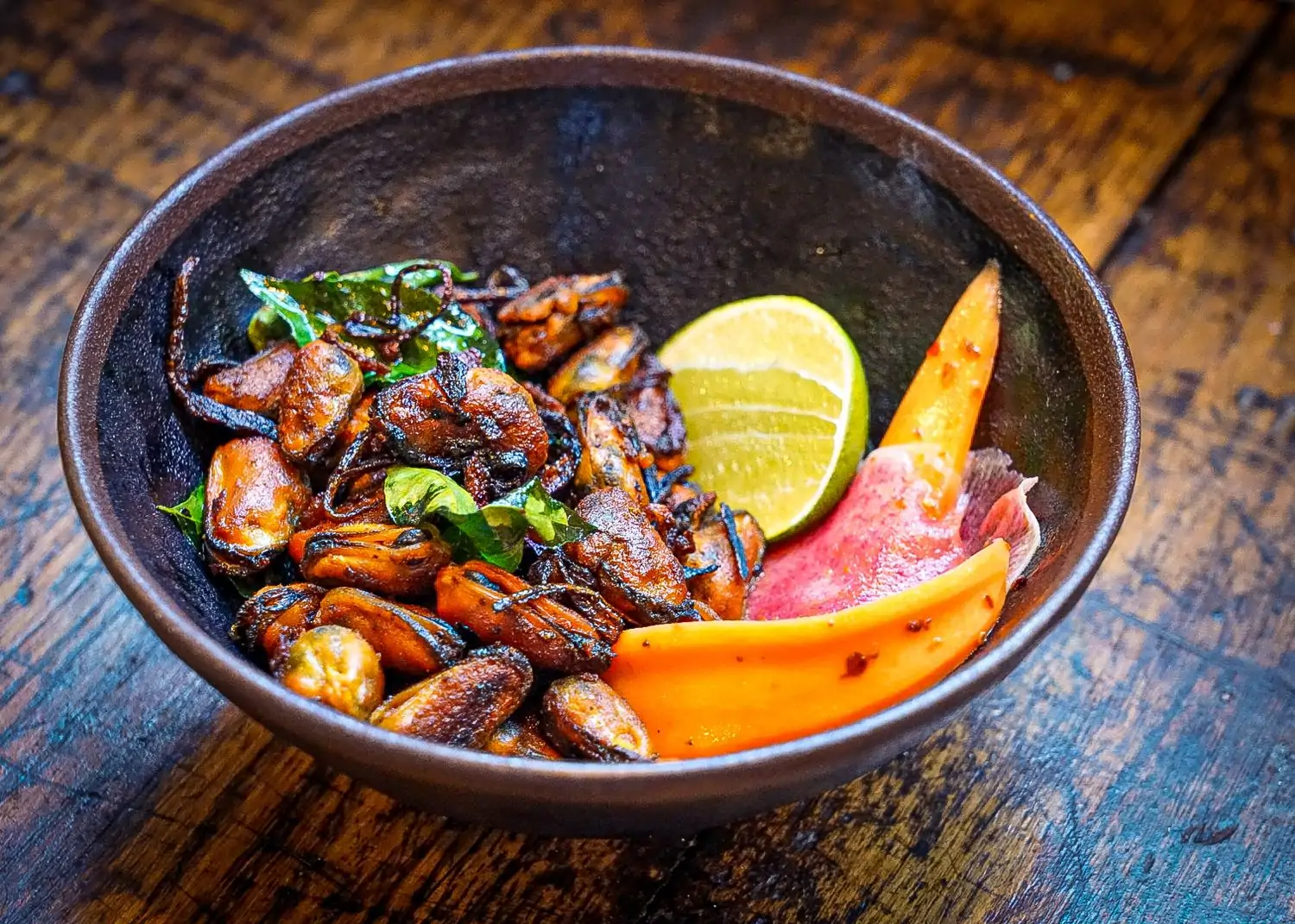 A ceramic bowl filled with pan-seared mussels with a carrot, lime, and radish garnish at Thattu, a restaurant in Chicago on OpenTable.