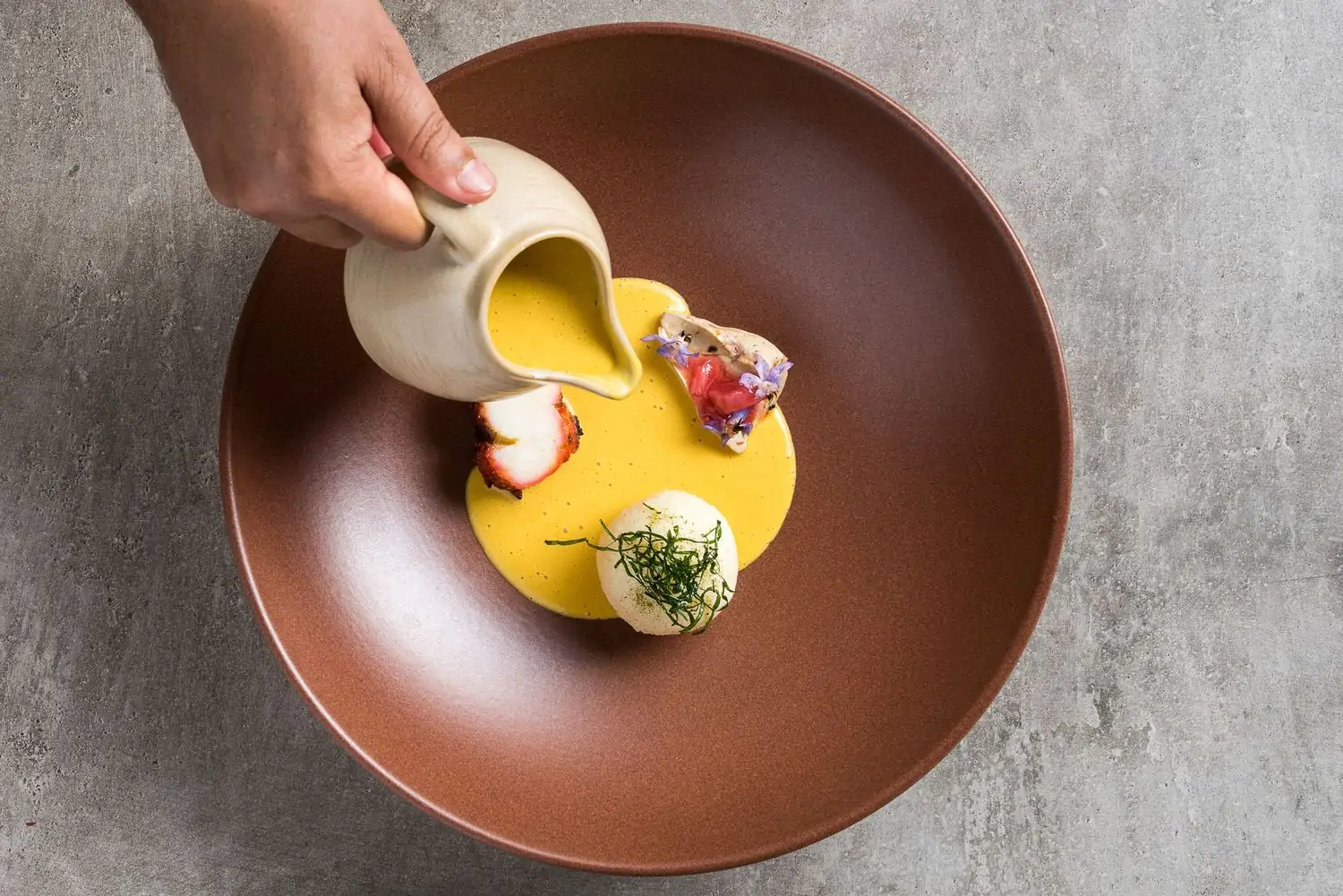 A hand pouring a creamy sauce into a brown ceramic bowl at ROOH Chicago, a restaurant on OpenTable.