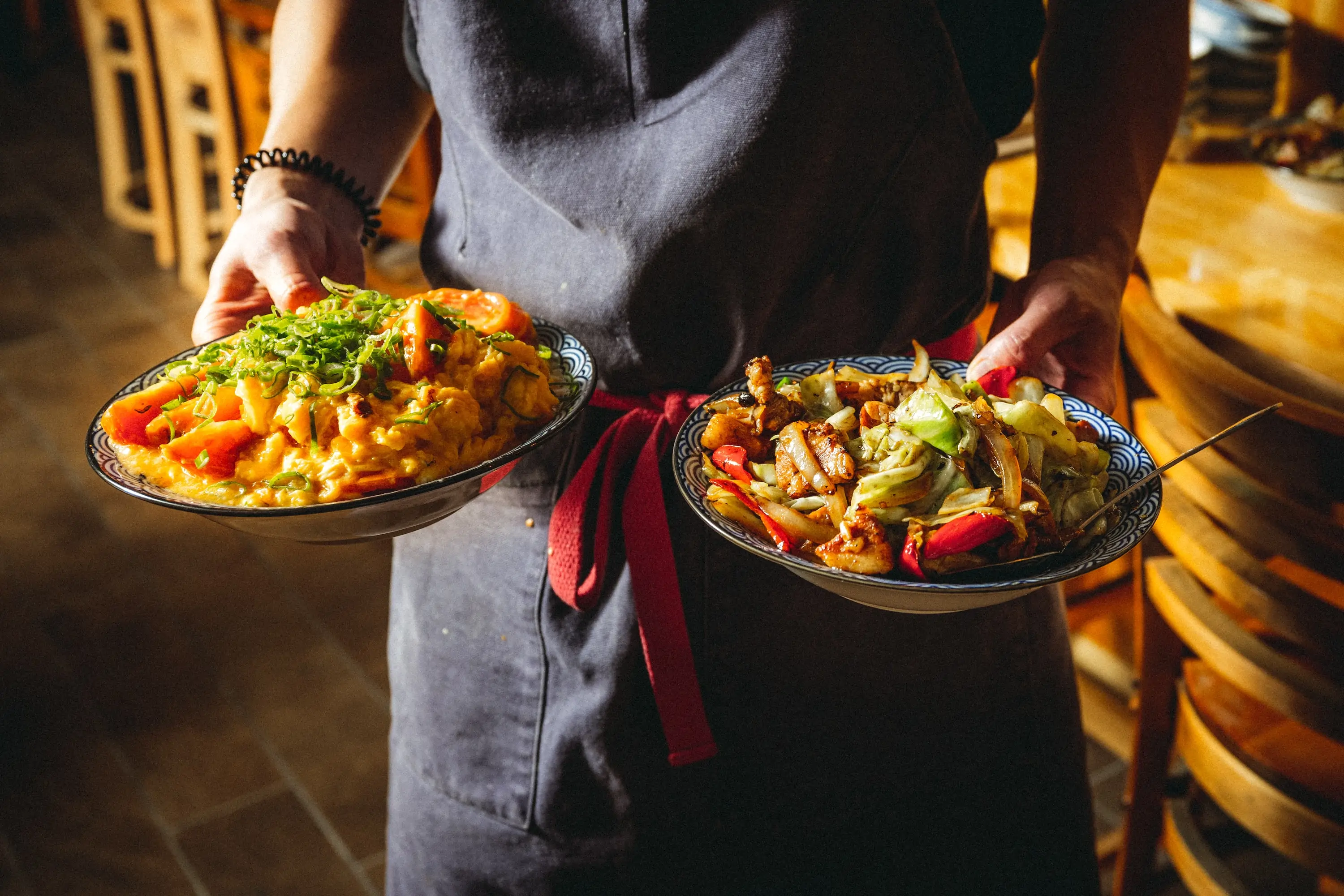 A pair of hands shown holding two plates of food at San Francisco restaurant Four Kings
