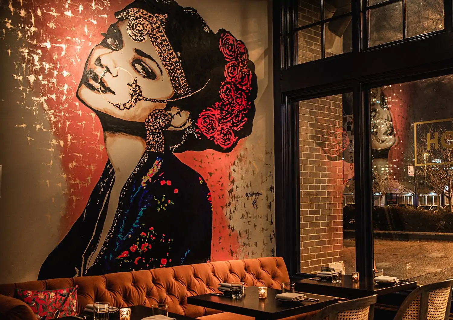A red, black, and gold mural of an Indian woman and a red velvet sofa at ROOH Chicago, a restaurant available on OpenTable.