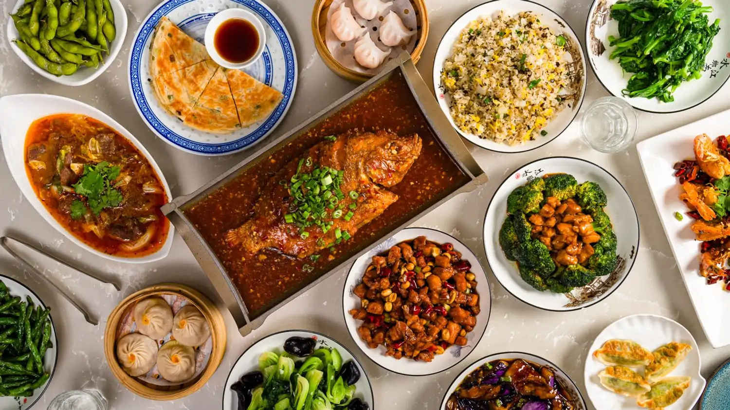 Covering a white table, an array of Sichuan dishes includes whole fish, dumplings, rice, green vegetables, and an assortment of meat and seafood at HUPO, one of the best Chinese restaurants in NYC, found on OpenTable.
