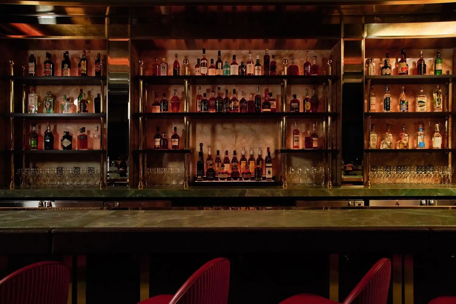 A brass-top bar with red velvet seats and open shelves of bottles behind it at The Alston, one of the Chicago best new restaurants on OpenTable.