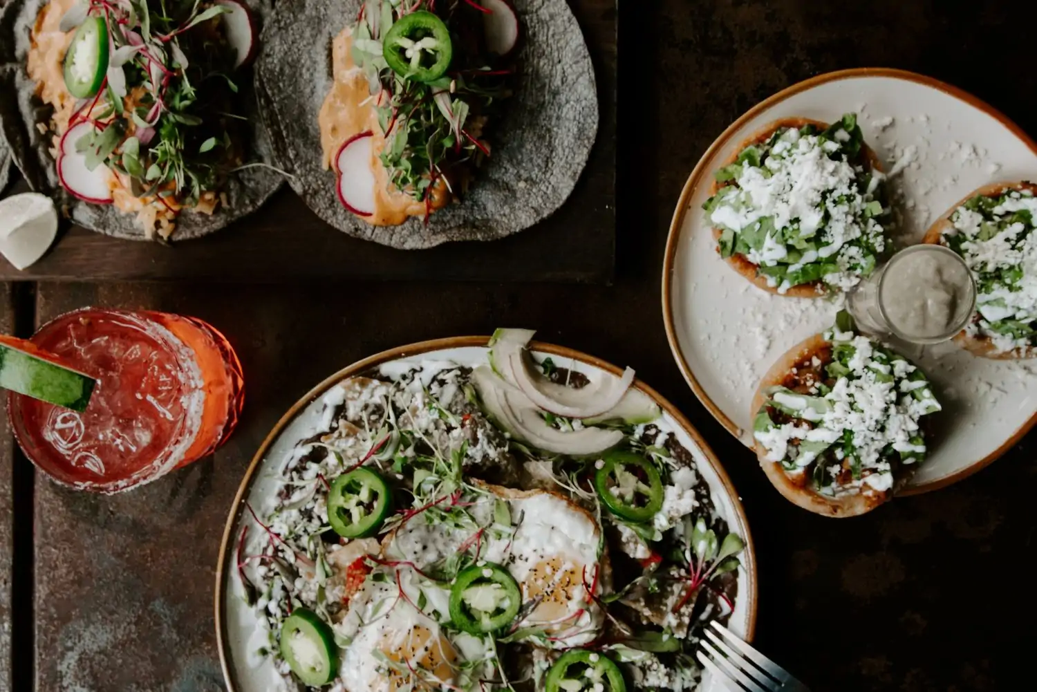 A table is set with Mexican dishes, including tacos, huevos rancheros, and a margarita, on a dark table at Maderas - Kitchen & Cantina, one of the best Mexican restaurants in Houston on OpenTable.