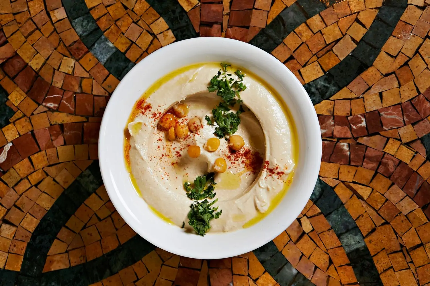 An overhead view of a bowl of hummus garnished with olive oil, sitting on a mosaic tabletop at Lebanese Taverna, one of the best vegetarian restaurants in DC, on OpenTable.