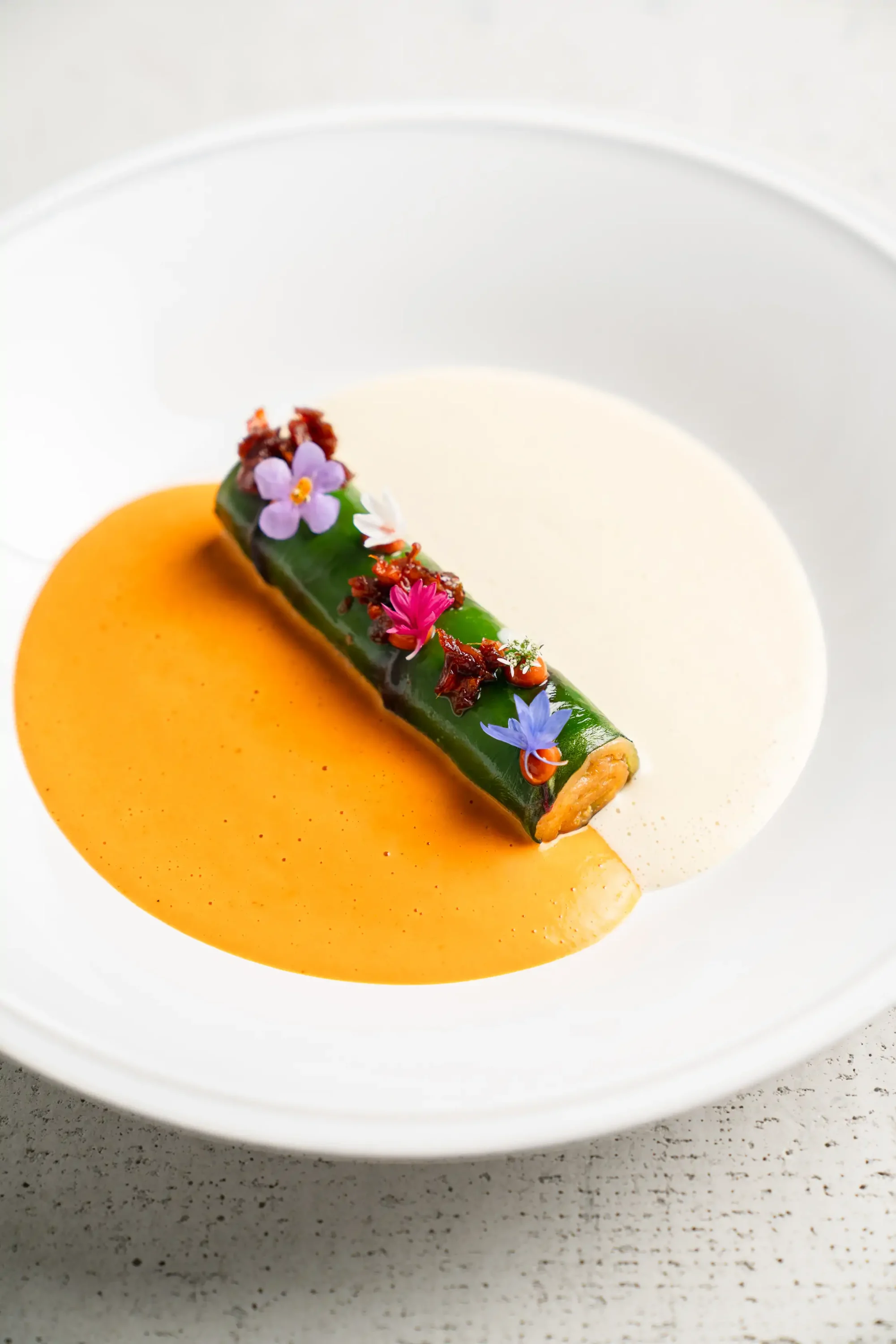 A paneer roulade covered in edible flowers surrounded by yellow sauce on a white bowl at Indienne in Chicago, one of the best date restaurants on OpenTable.