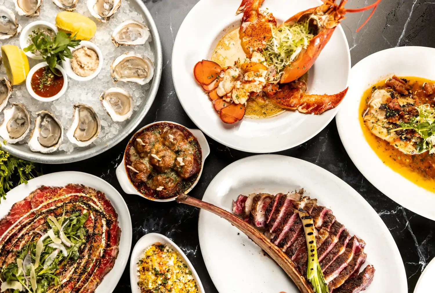 A table set with plates of lobster, seared and sliced steak, meatballs, oysters, and other items at Town Hearth, one of the best steak restaurants in Dallas, on OpenTable.